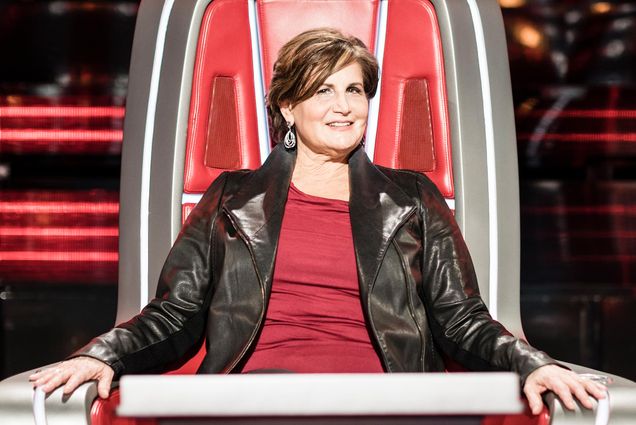 Photo of Brooke Karzen (CFA’84) with a leather jacket and red shirt on in one of the judge chairs from the show The Voice.