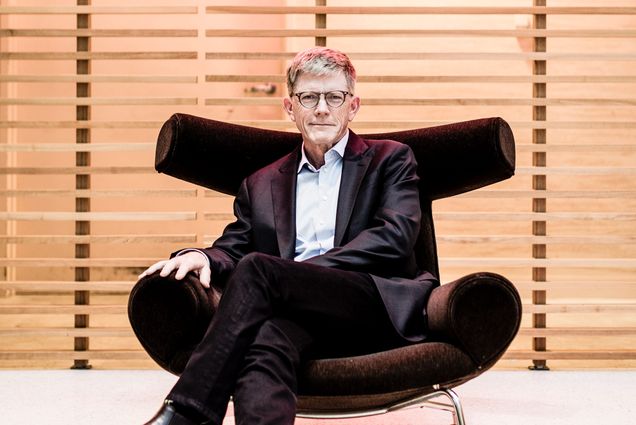 Portrait of Jay Roewe (COM’79) in a black suit in a stylish black chair. Behind him, a neon sign reads "HBO"