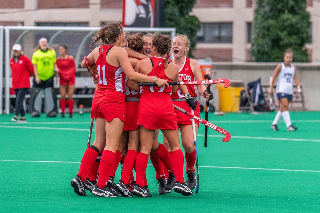 Field hockey team, dressed in red jerseys, celebrates as a group, during a game.