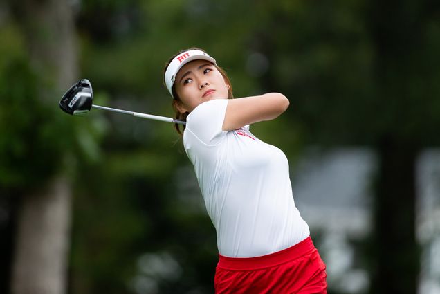 Women’s golf team member Zhangcheng “Kristy” Guo at the end of her golf swing. She wears a white shirt and hat.