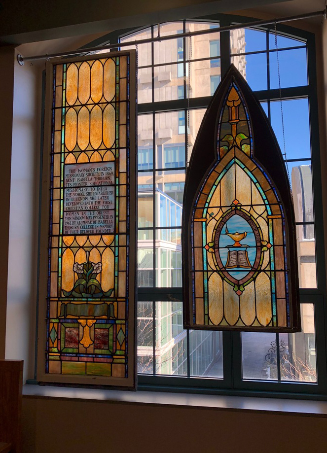 Photo of STH’s library which now features a stained glass window memorializing the founding members of the Woman’s Foreign Missionary Society of the Methodist Episcopal Church. The stained glass window is a gothic shape, made primarily of golden glass.