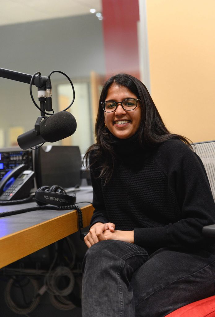Photo of Sarika Ram (CAS’21) in a black shirt and pants in a podcast recording studio, presumably recording her podcast Criminalized.