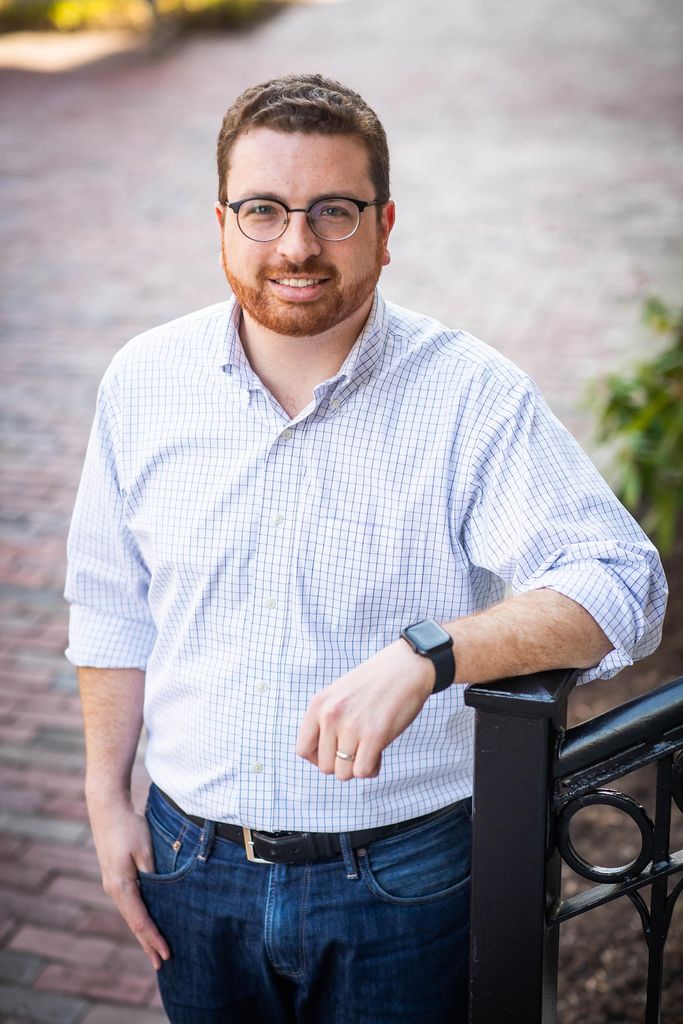 Political scientist Maxwell Palmer in a buttondown shirt with his hand resting on a stair railing.