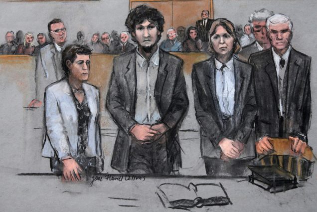 In this courtroom sketch, Boston Marathon bomber Dzhokhar Tsarnaev, center, stands with his defense attorneys as a death by lethal injection sentence is read at the Moakley Federal court house in the penalty phase of his trial in Boston, Friday, May 15, 2015. Tsarnaev, center holds his hands in front of him and looks sternly, the court room occupants are seen behind him.