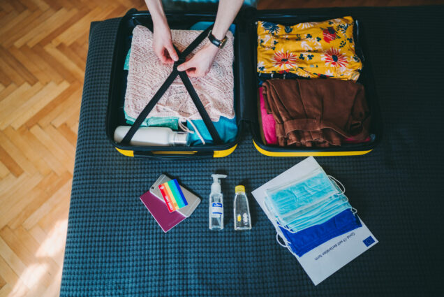 A photo of a person packing a suitcase with items including masks and hand sanitizer