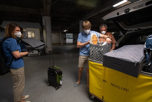 Matthew Curtis (Questrom’24) (center), with help from his mother, Klara, and father, Rod, moving into Warren Towers August 17. Curtis pulls a plastic basket from a yellow cart from the back of a car in a parking garage.