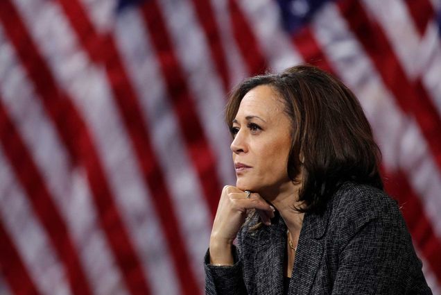 California Senator Kamala Harris sitting in front of United States flags with her chin resting on her hand.