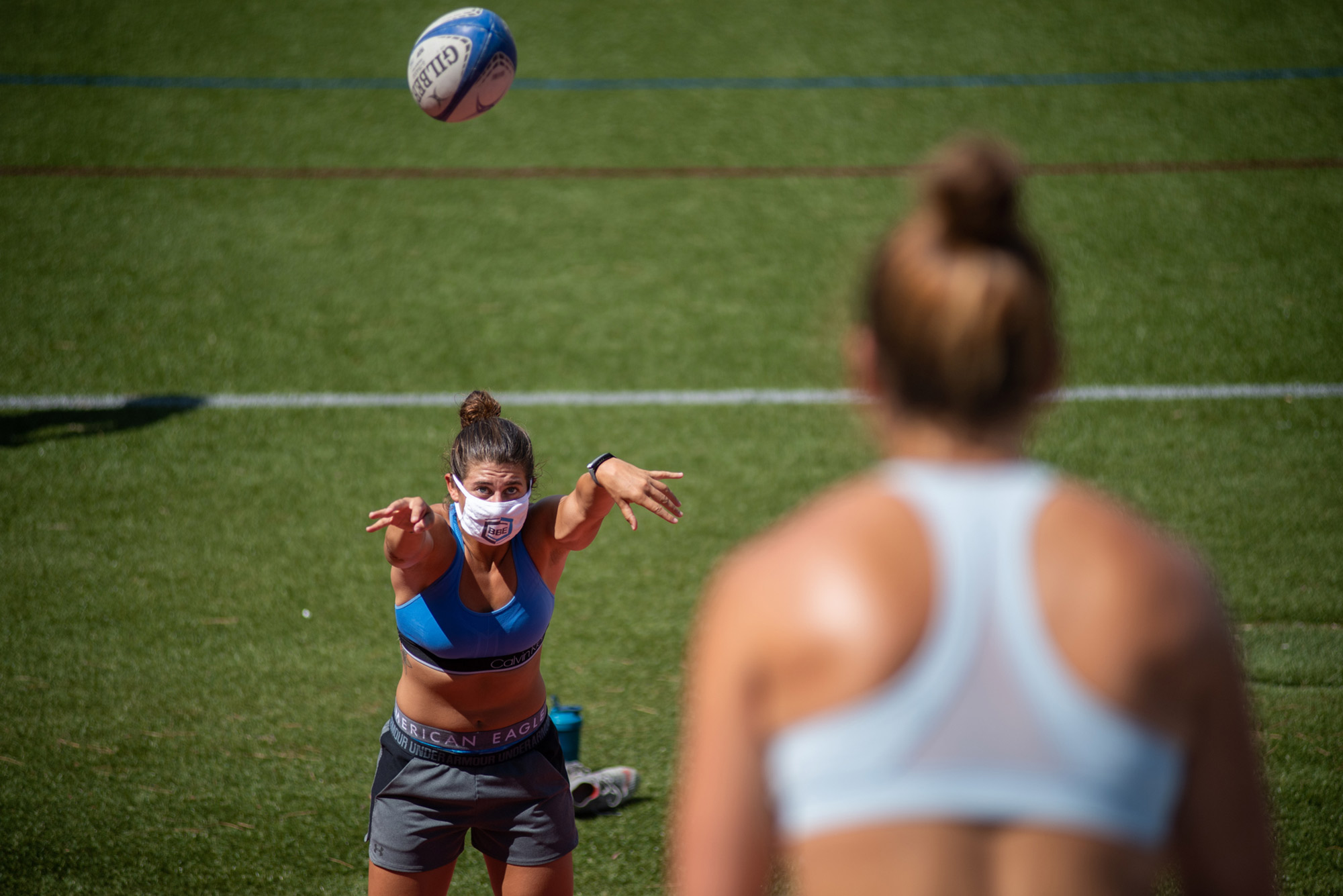 Paige Stathapoulos (CAS’16) wears a mask tosses a rugby football to her Rugby teammate Jenny Kronish at Nickerson field on the West Campus move in August 28. The rugby football is seen in flight.