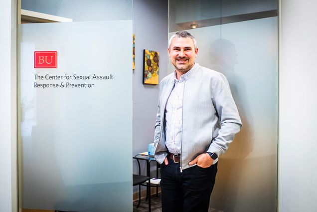 A photo of Nathan Brewer standing in front of a sign that reads "Center For BU Sexual Assault Response & Prevention"