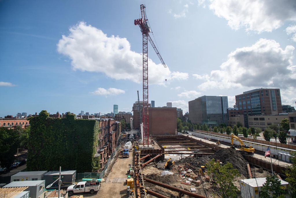Photo of continued construction at Data Services Center, including the addition of a massive red crane that cuts in the city skyline. Work trucks and metal beams are seen around the construction site.