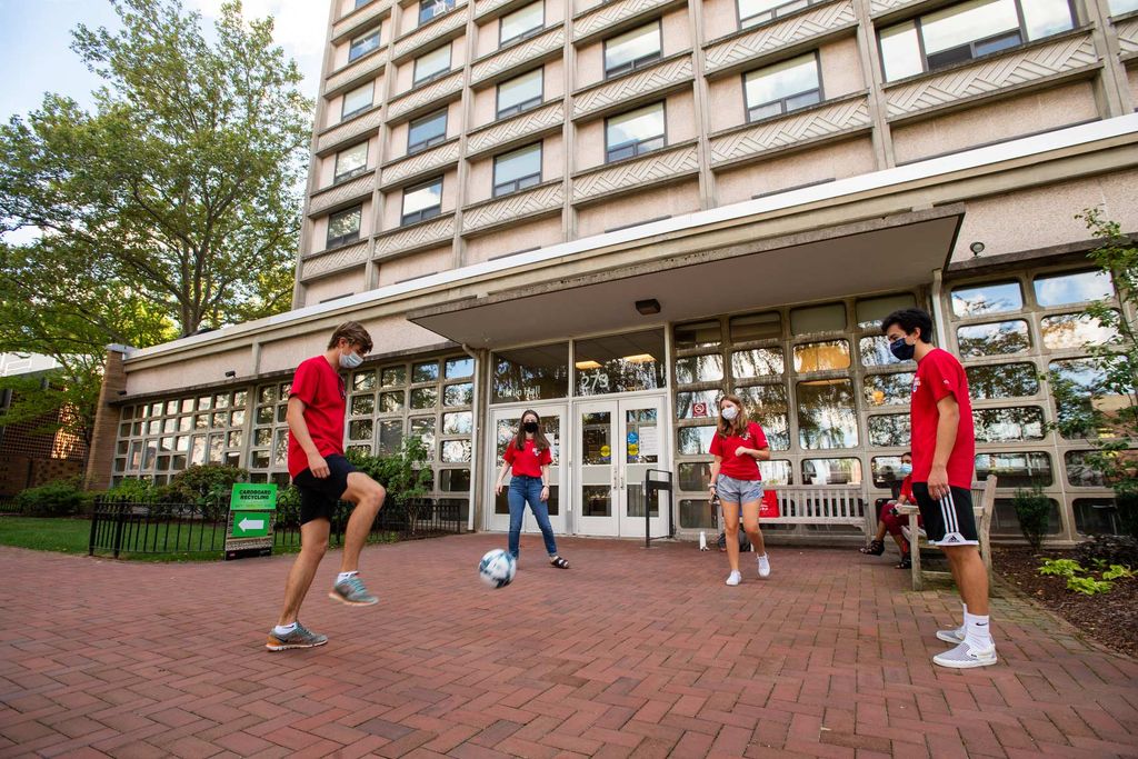 Scarlet Squad members Charlie Courtemanche (CAS’22) (from left), Katelyn Sylvester (CAS’23), Morgan O’Brien (Sargent’22), and Kyle Chin pass a soccer ball (COM’22), while Musfika Mishi (CGS'21) sits on the bench, passing the time while waiting to assist students moving into Claflin Hall on August 18. All of the students wear red shirts.