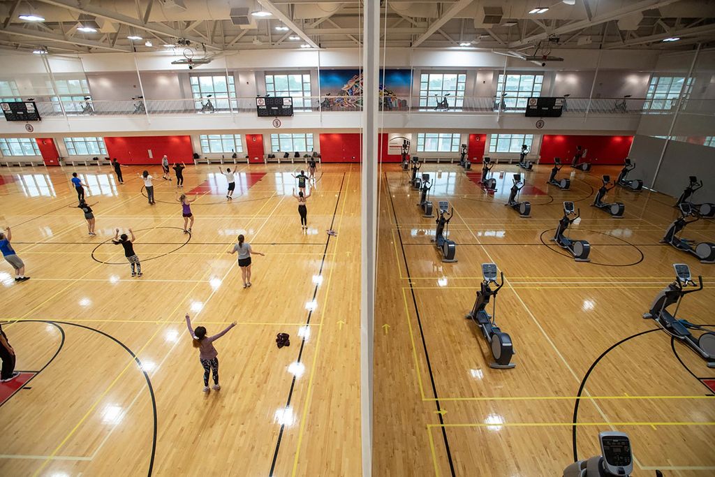 Photo from the top of the gym looking down as roughly 40 students, spaced out in 14-foot squares marked off by yellow tape, participate in fitness instructor John O’Brien’s boxing class at FitRec Gym 3 September 3. On the right, on the other side of a divider, Rows of empty elliptical machines are seen.