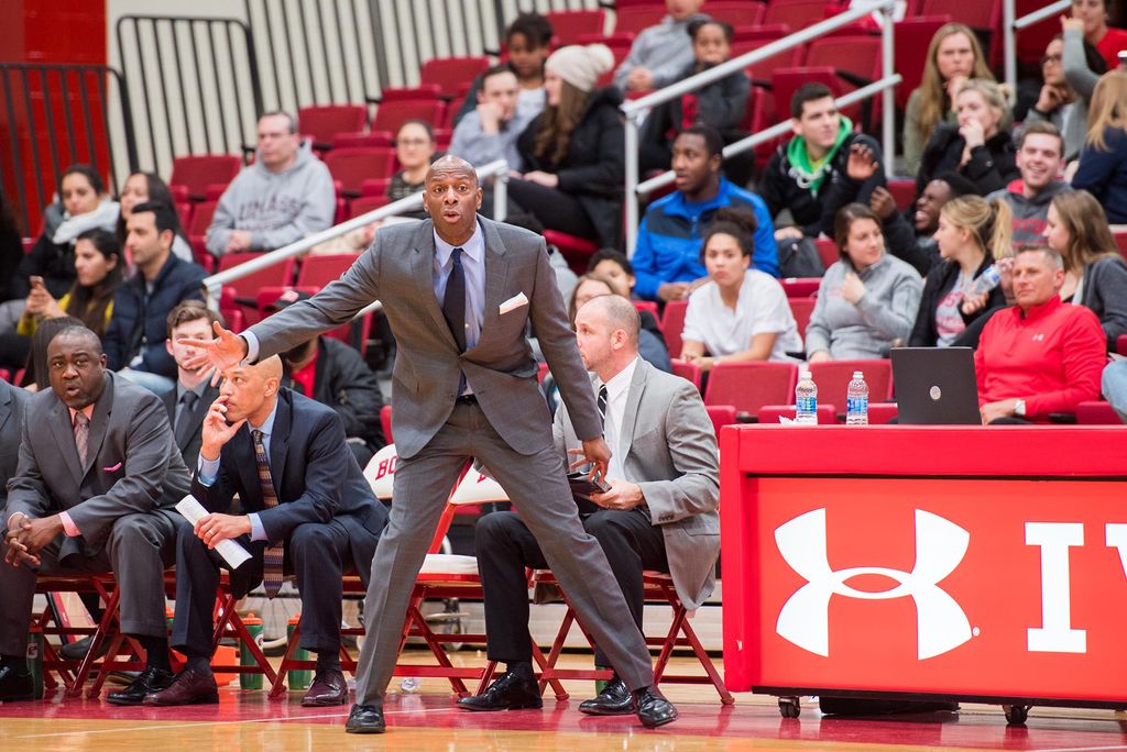 Photo of Coach Joe Jones during a home game against Loyola played ay Case Gym January 31, 2018. BU defeated Loyola 64-55. In the photo, Jones stands in a suit at the edge of the court and motions to players. A crowd sits behind him in the bleachers.