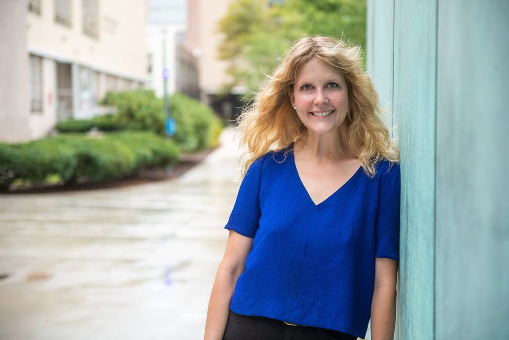 A photo of Meghann Lucy standing in a blue shirt smiling