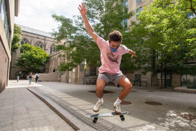 Photo of Alvaro Mendoza (ENG’22) works on his skateboard practicing tricks near LAW on August 31. He wears a pink shirt and gray shorts and is seen mid-air while doing a trick.