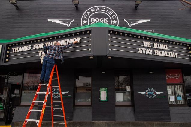 Photo of the facade of Paradise Rock Club in Boston. An employee stands on an orange ladder to change the letters of the marquee. The right marquee reads "be kind, stay healthy"