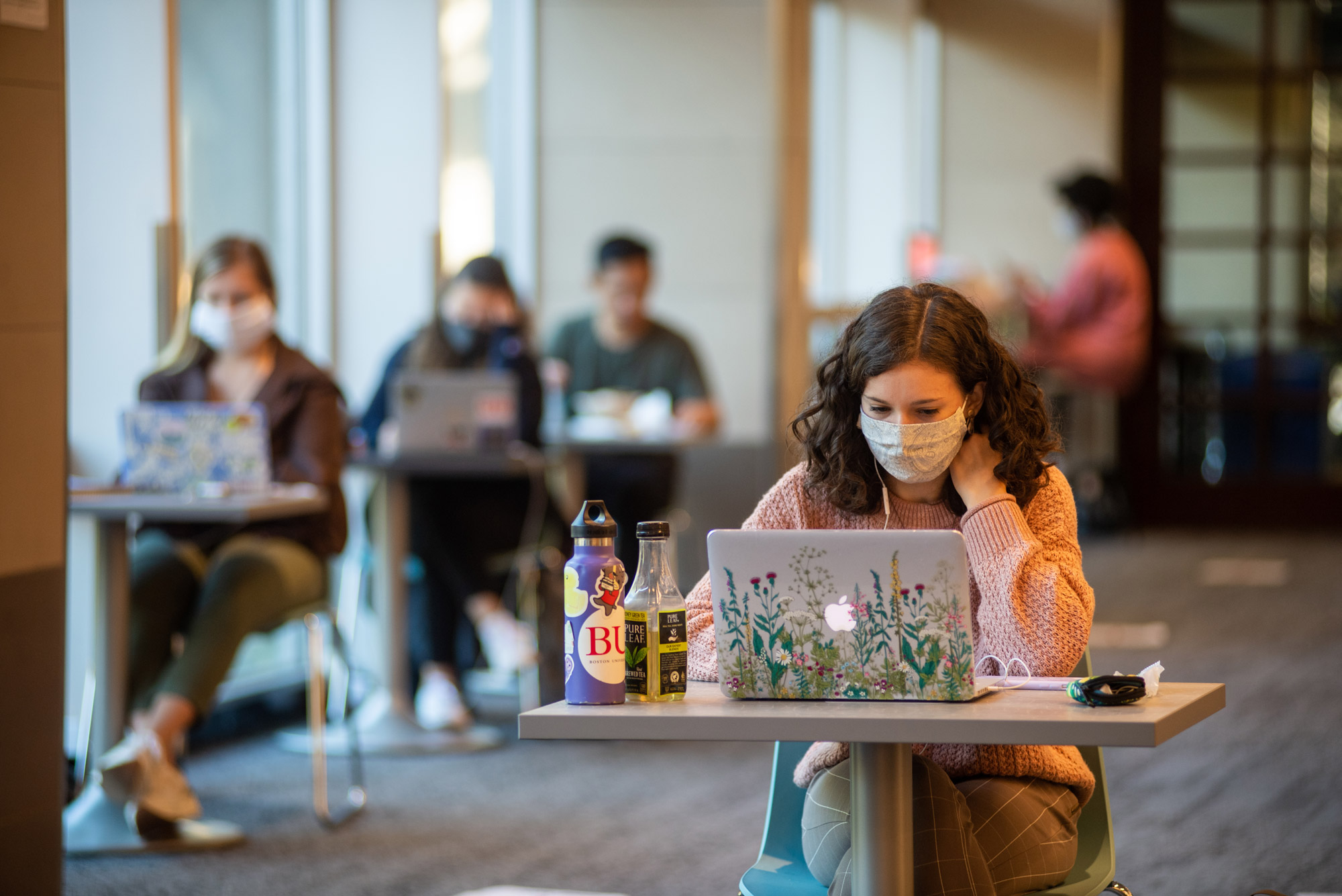 A photo of a student sitting at their computer wearing a mask