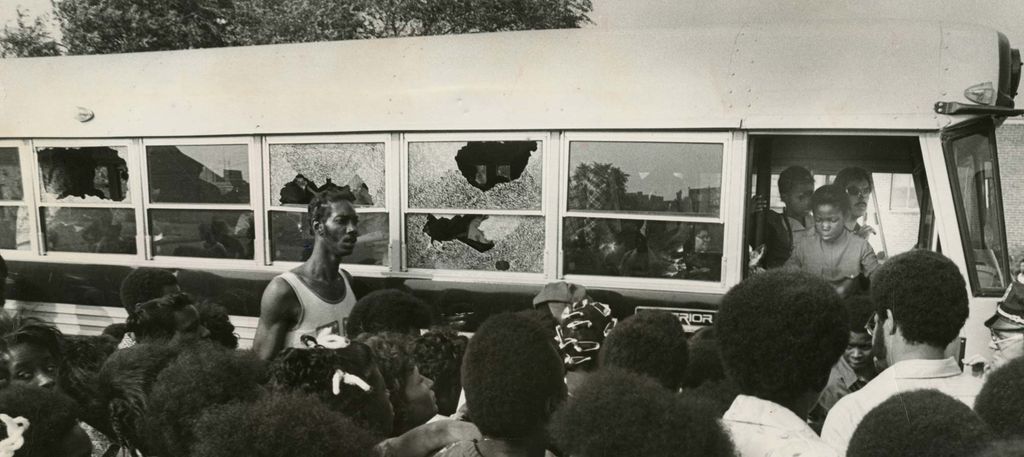 A crowd watches as a bus carrying students returns to Columbia Point with broken windows on Sept. 12, 1974, the first day of school under the new busing system put in place to desegregate Boston Public Schools.