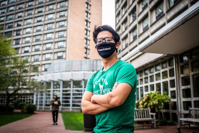 Photo of Dragon Ding (CAS 21) an RA in Sleeper Hall posing for a photo on West campus on October 5, 2020. Ding wears a black face mask that reads "West is Best" and has a green BU shirt on.