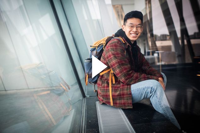 A photo of Joshua Pei smiling at the camera. A white video play button sits over the image.