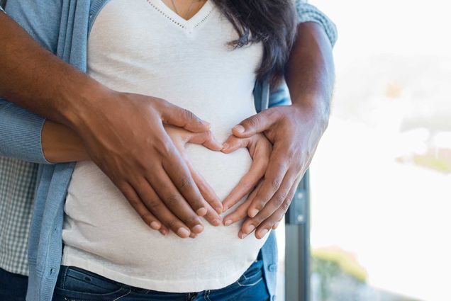A pregnant African American couple place their hands over the womb