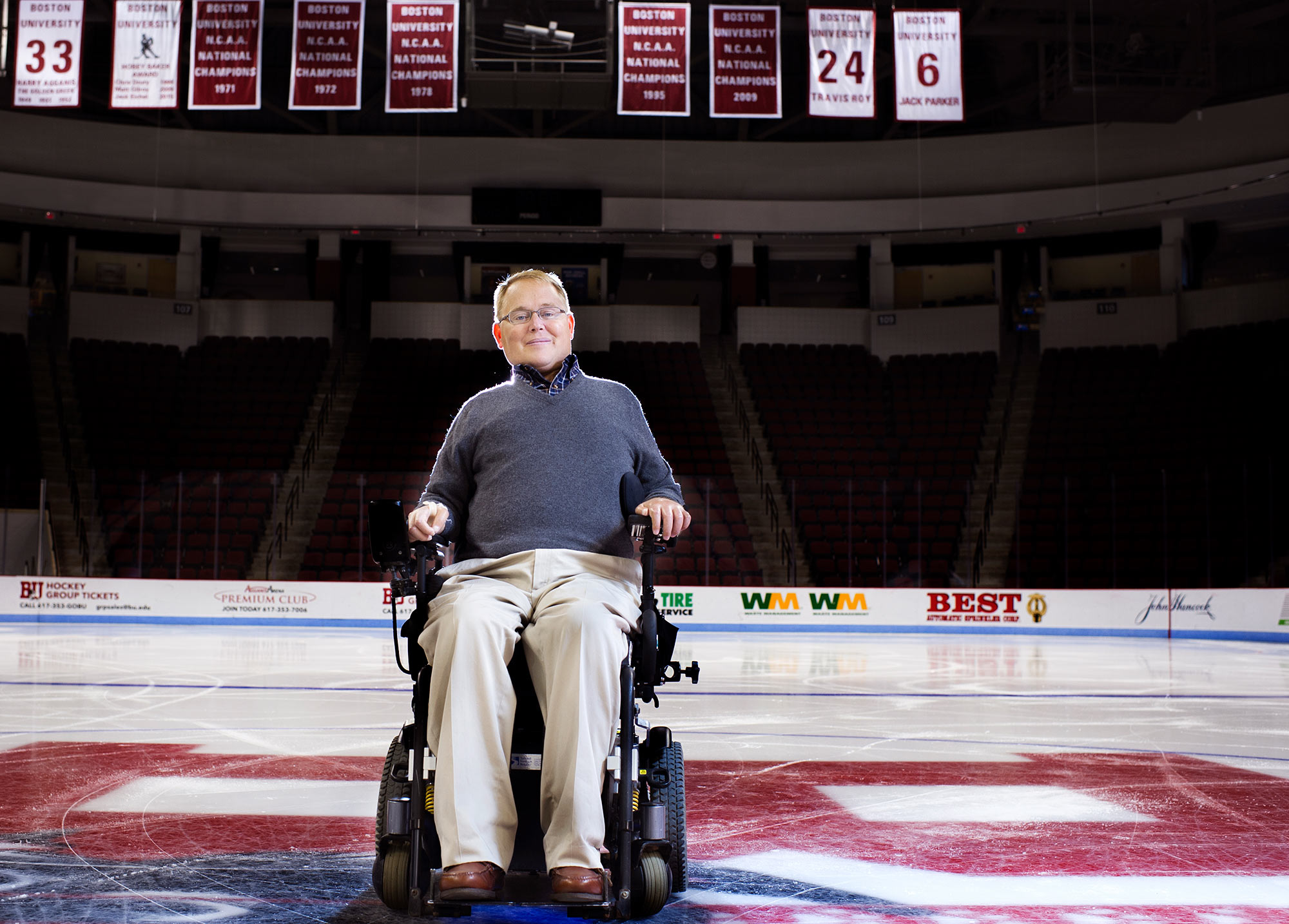 Photo of Travis Roy on Monday, October 6, 2015 at center ice of the Agganis Arena. He wears a grey sweater and his retired jersey number, 24, is seen hanging from the ceiling.