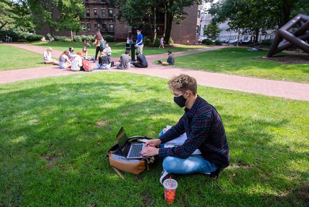 Photo Quinn Wilson (CAS’21) sitting on the ground and studying for his French class on BU Beach September 14. A dunkin donuts cup sits to his left. A class sitting in a circle is seen behind him.