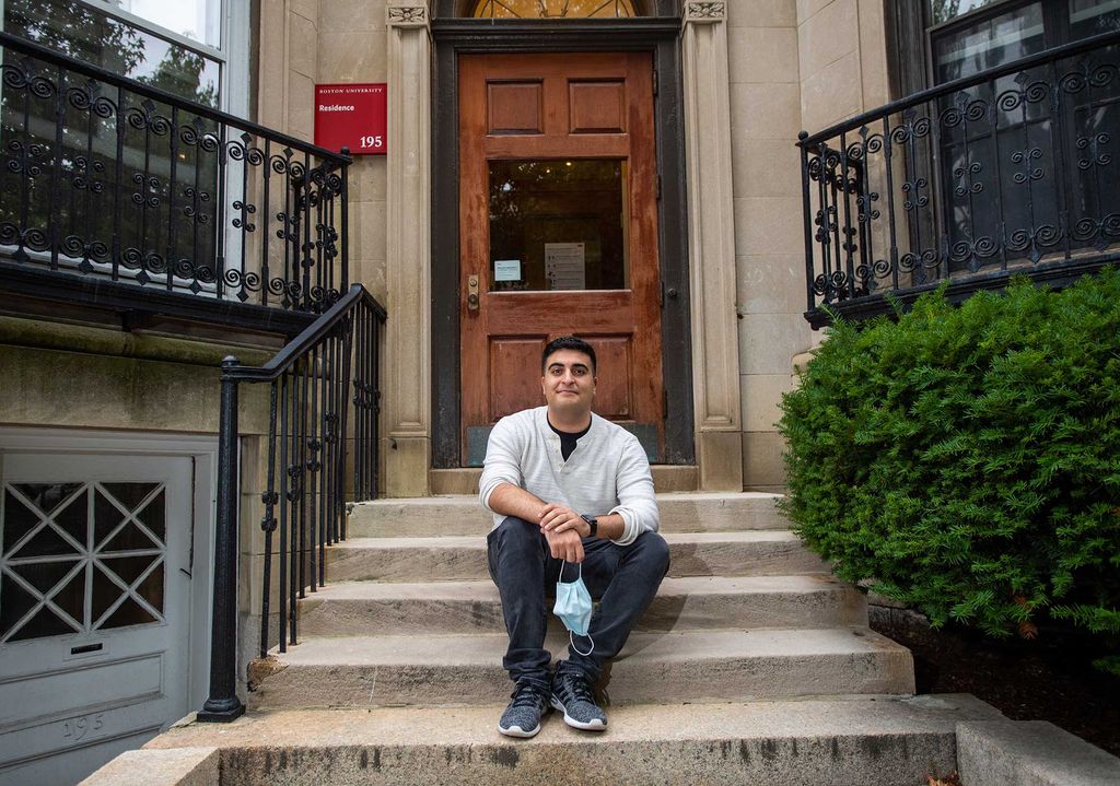 Photo of Resident Assistant Nathan Simani (CAS’21) at his Bay State Rd residence. He sits on the steps and holds a blue face mask in his hand.