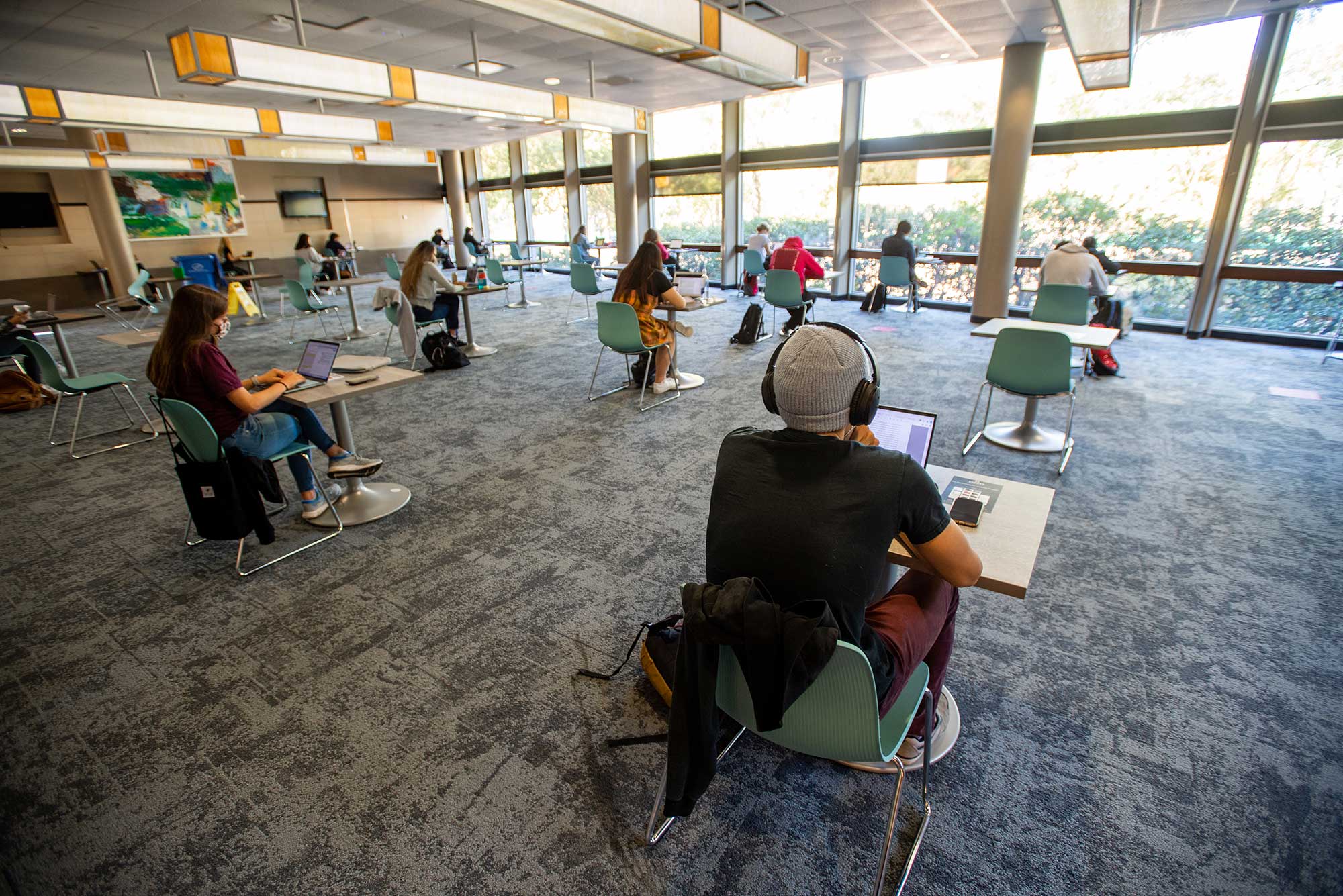 Photo of students studying while socially distanced in the Back Court in the GSU October 14, 2020. There are about a dozen or so students seen who work on their laptop all facing the windows at the back of the room.
