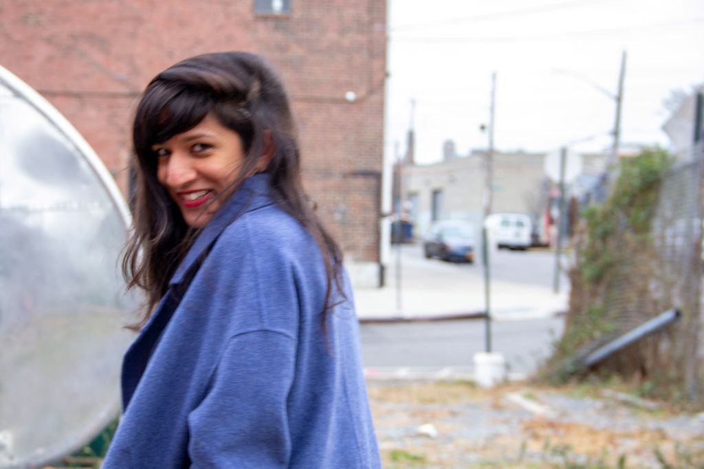 Stylishly blurry photo of Megan Fernandes (GRS’12) in a light blue sweater. A brick building is seen in the background.