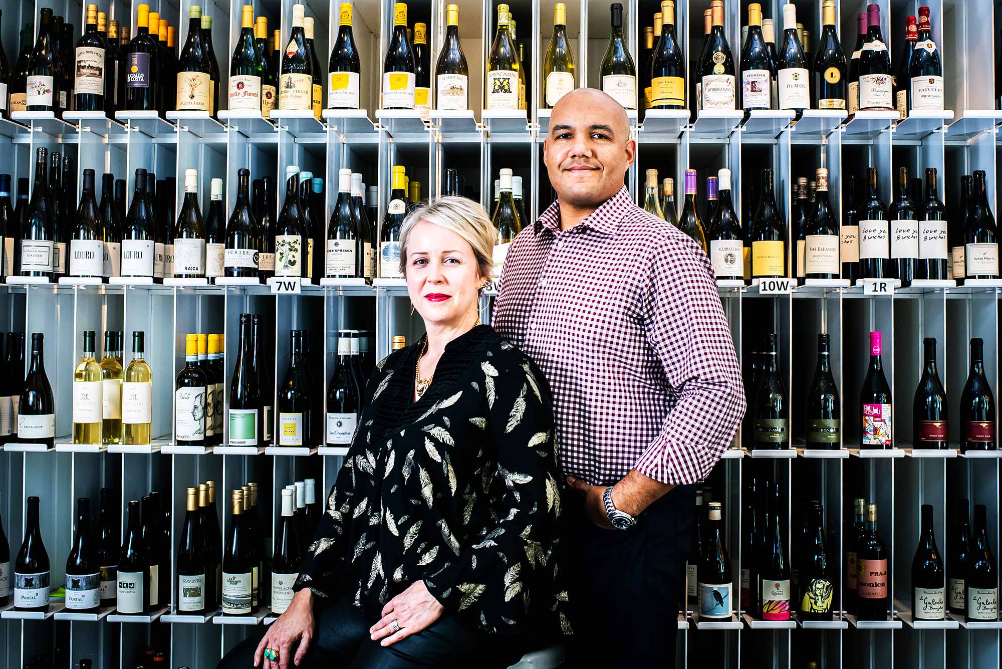 TJ and Hadley Douglas, owners of Urban Grape in Boston, pose for a photo on November 2, 2020. A floor to ceiling rack of wine bottles is seen behind them.