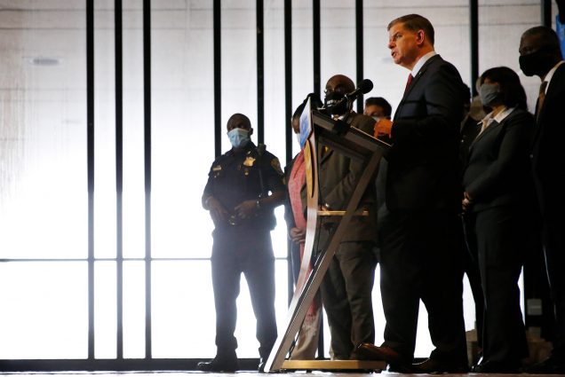 Photo of Mayor Martin J. Walsh speaking at a press conference at Boston City Hall in Boston, flanked by members of the Boston Police Reform Task Force, as he announces a plan for a slate of reforms to the Boston Police Department on Oct. 13, 2020. Walsh stands at a podium on the right of the photo, with the reform task around him.