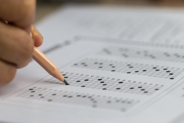 Photo of a hand of a student holding a pencil while testing filling out a standardized test answer sheet.