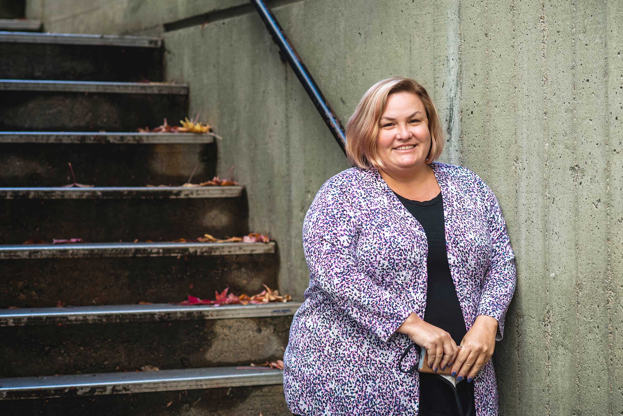 Photo of Amy Goodrich, director of catering at BU, in a colorful sweater posing at the bottom of a staircase.