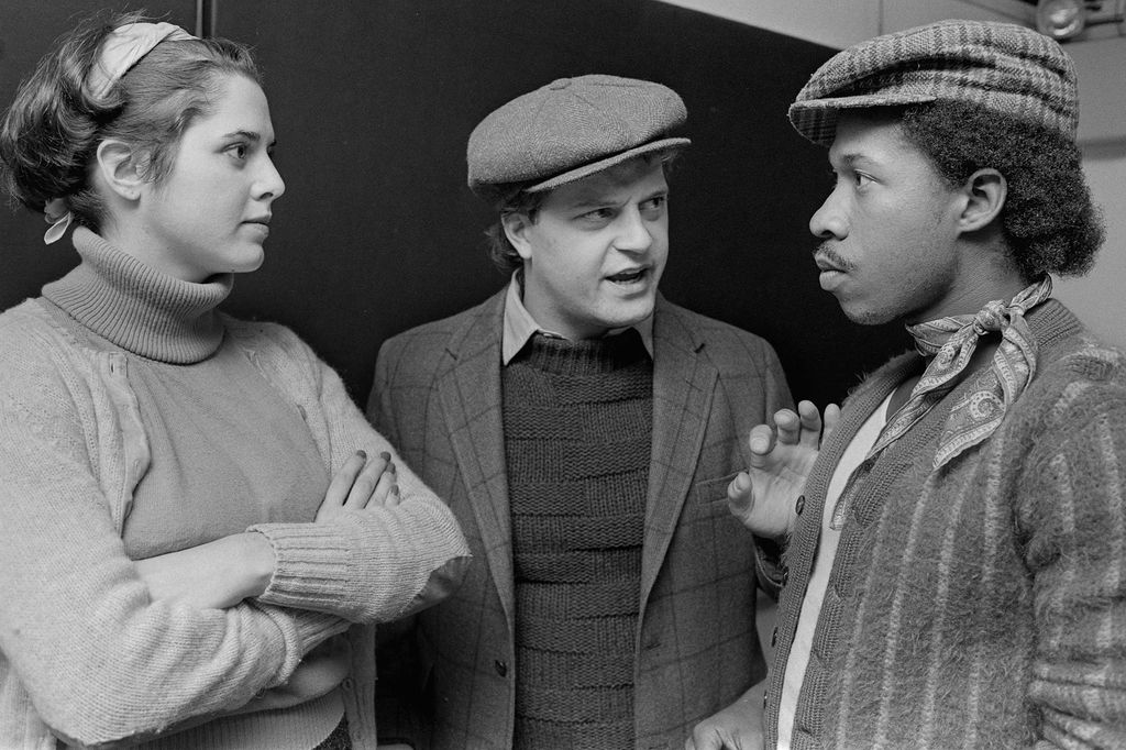 Black and white photo of Chiklis (center) at a rehearsal for a 1984 BU mainstage production of The Hostage. A woman with her arms crossed and a man in a fedora stand to his left and right.