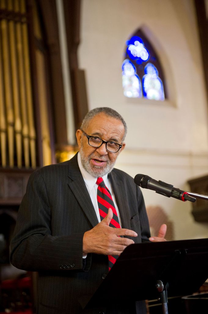 Photo of Rev. Gil Galdwell (GRS’55, Hon.’59) speaking at a podium in what looks like a church, with a suit and red tie on.