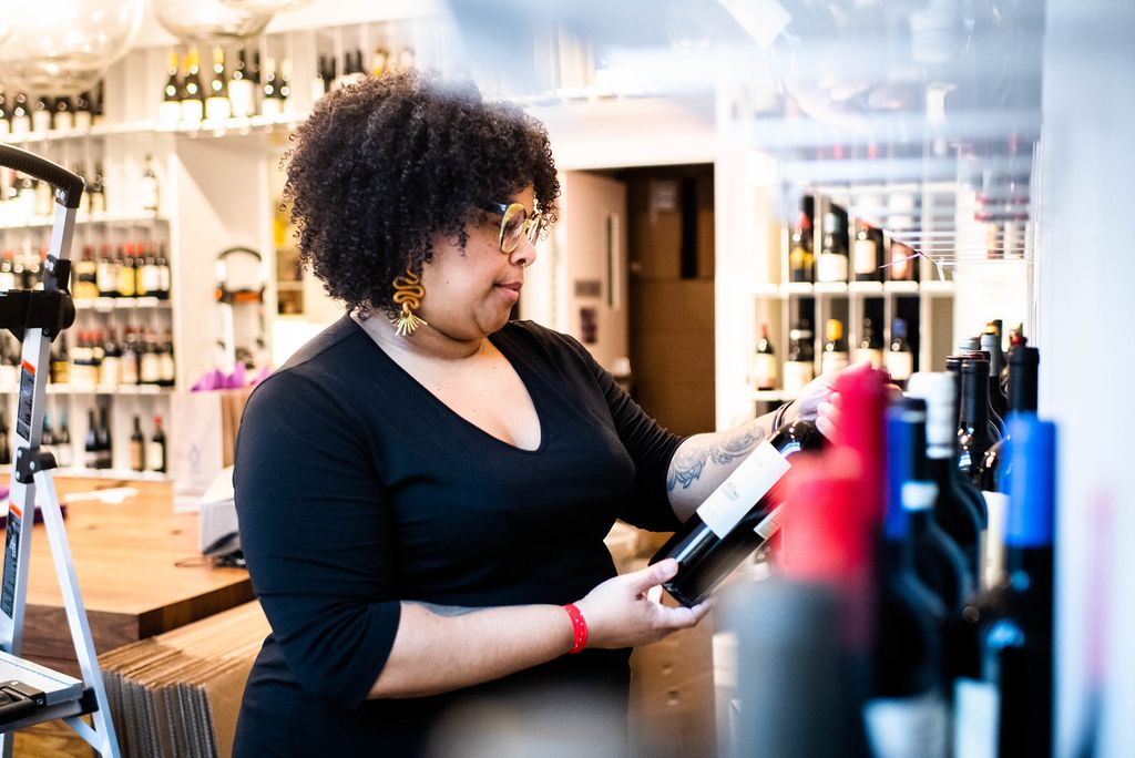 Suhayl Ramirez,a student in the BU Wine Program works at Urban Grape on November 11, 2020. She holds a wine bottle and reads the label.