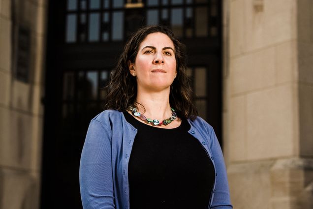 Portrait of Wheelock College Associate Professor, Kathleen Corriveau, standing outside what looks like the entrance to a church in shale blue sweater and black dress.