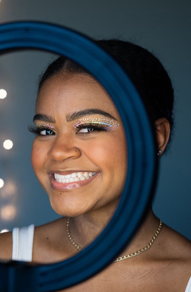 Photo of Tatyana F. Da Rosa (CAS’20, Questrom’21) smiling wide in front of ring light. Da Rosa's Hobby is makeup and makeup tutorials; she is sporting a rainbow-colored eye shadow design.