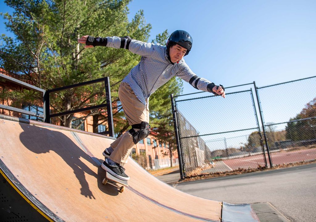 Photo of Scott Bunch, College of Engineering associate professor of mechanical engineering, materials science and engineering, skateboarding down a skate ramp with a helmet and pads while wearing khakis and a button down. 