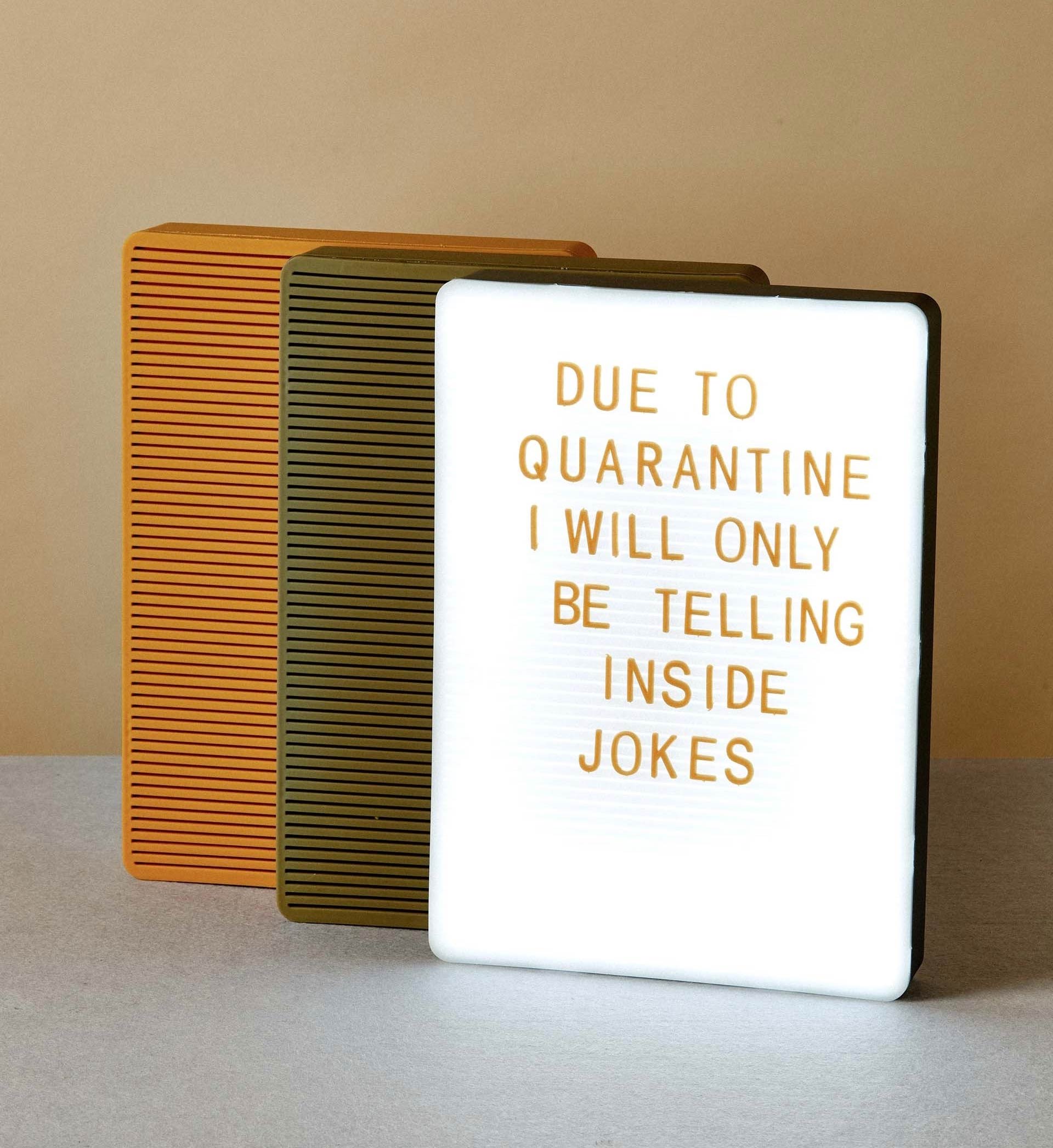 Photo of a pegboard sign that reads in orange removable characters “DUE TO QUARANTINE I WILL ONLY BE TELLING INSIDE JOKES” with two other closed green and orange signs behind it.