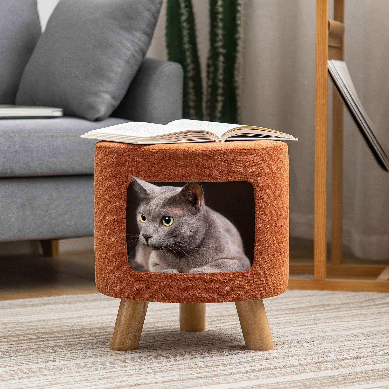 Photo of an ottoman with a pet cave, where a gray cat sits. Living furniture is seen in the background. 