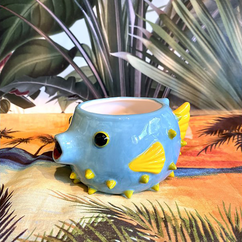 Photo of a pufferfish tiki mug on a colorful table with palm fronds.