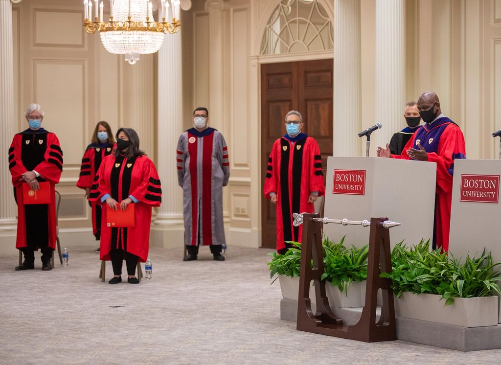Dean of students Kenneth Elmore takes to the podium in the Metcalf Ballroom for the virtual matriculation for the incoming class of 2024 at 1 Silber Way August 30. Behind him to his right stand others dressed in matriculation regalia.