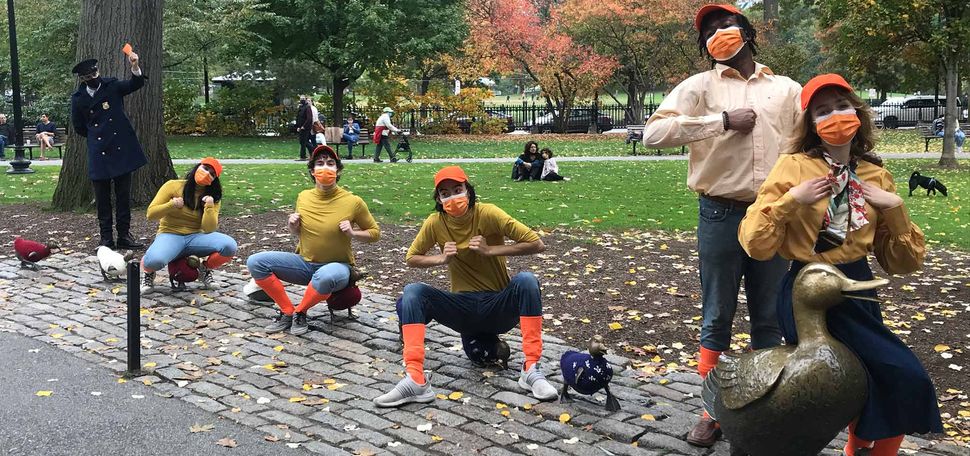 A photo of cast members sitting on the Make Way for Ducklings sculpture in the Boston Public Garden