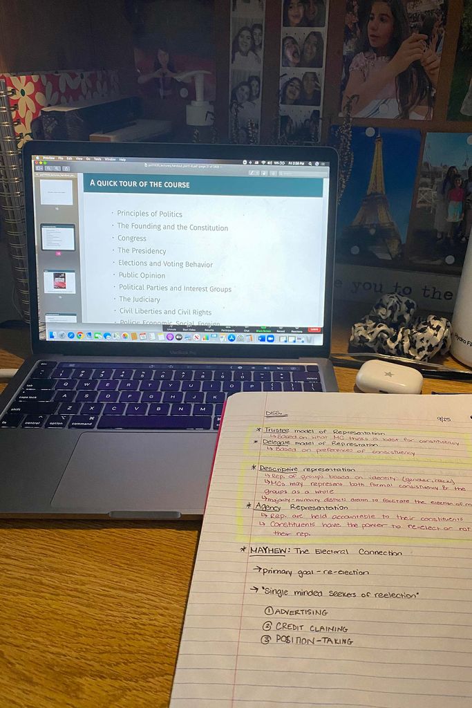Photo of a laptop with a slideshow that reads “A quick tour of the course” and a notebook on a table with pink and black ink. In the background, a cork board of photos is seen in shadow.