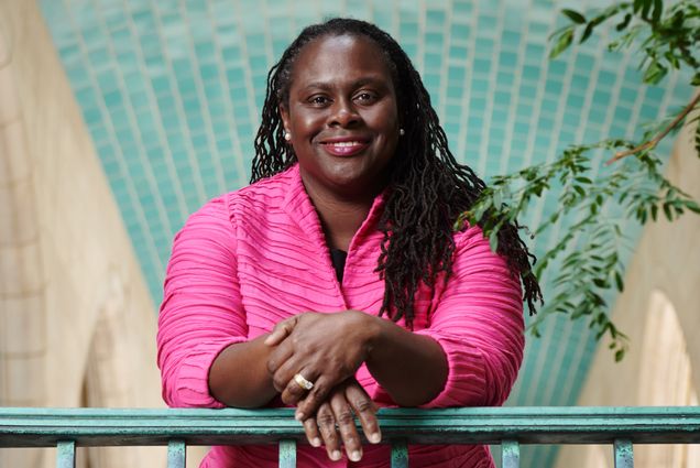 A portrait photo of Angela Onwuachi-Willig leaning against a railing with her hands crossed in front of her.