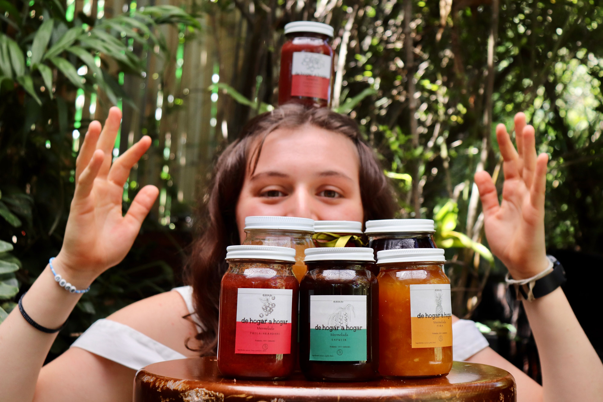 A photo of Inés Santacruz holding jars of jams and preserves up in front of her face. Several jars also sit on a table in front of her.