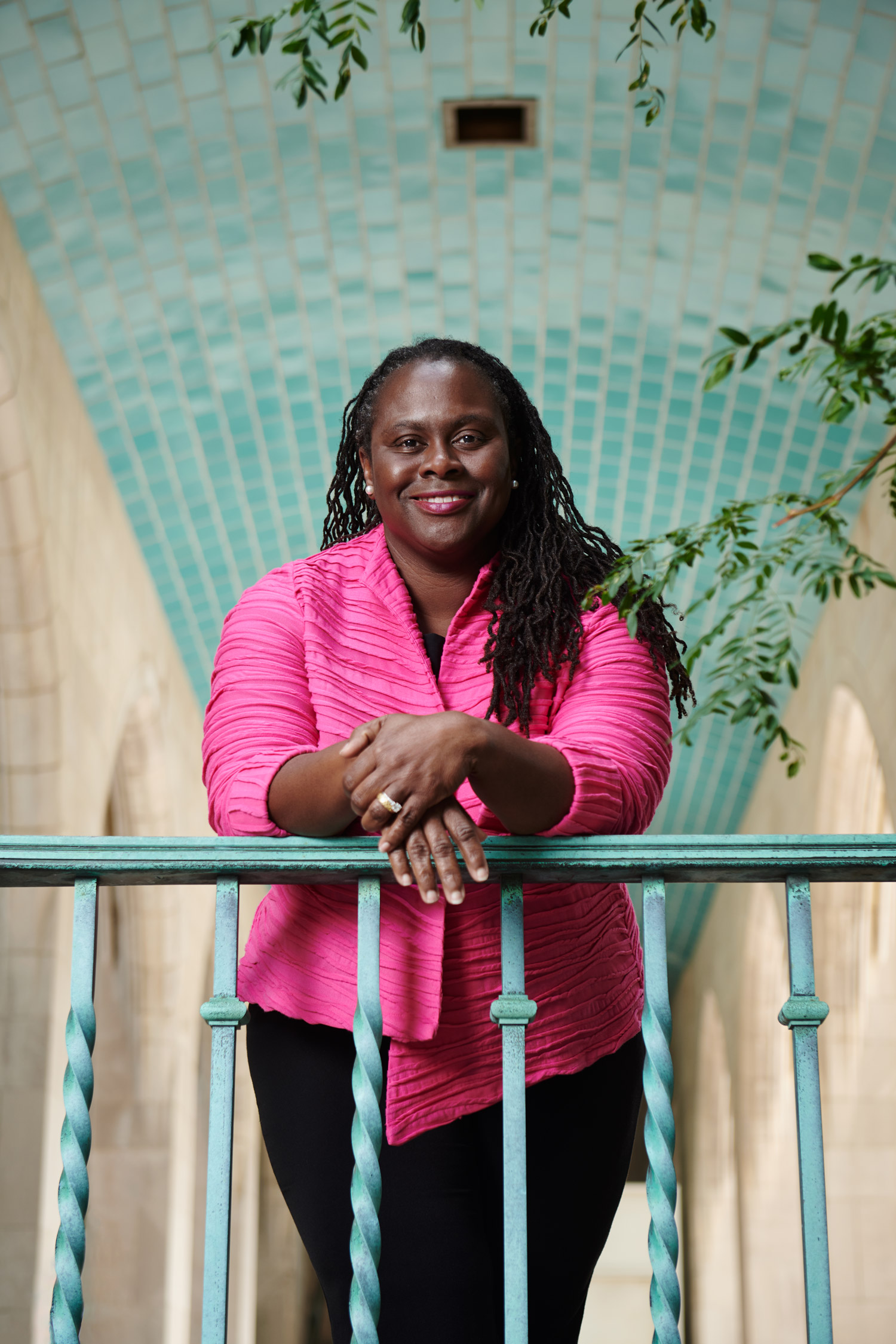 A portrait photo of Angela Onwuachi-Willig leaning against a railing with her hands crossed in front of her.