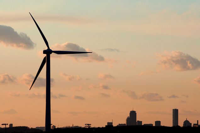 A photo of a wind turbine in front of Boston's skyline